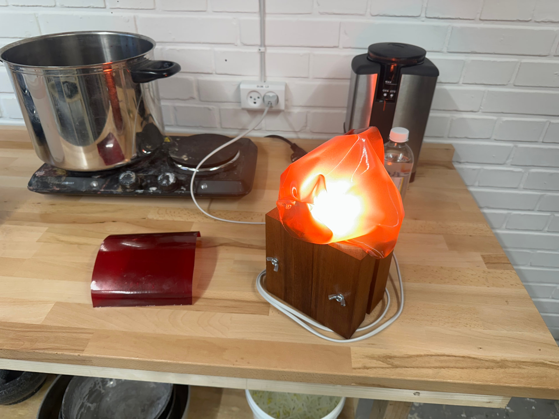A lamp with a translucent red bioplastic shade glowing on a wooden base in the workshop.