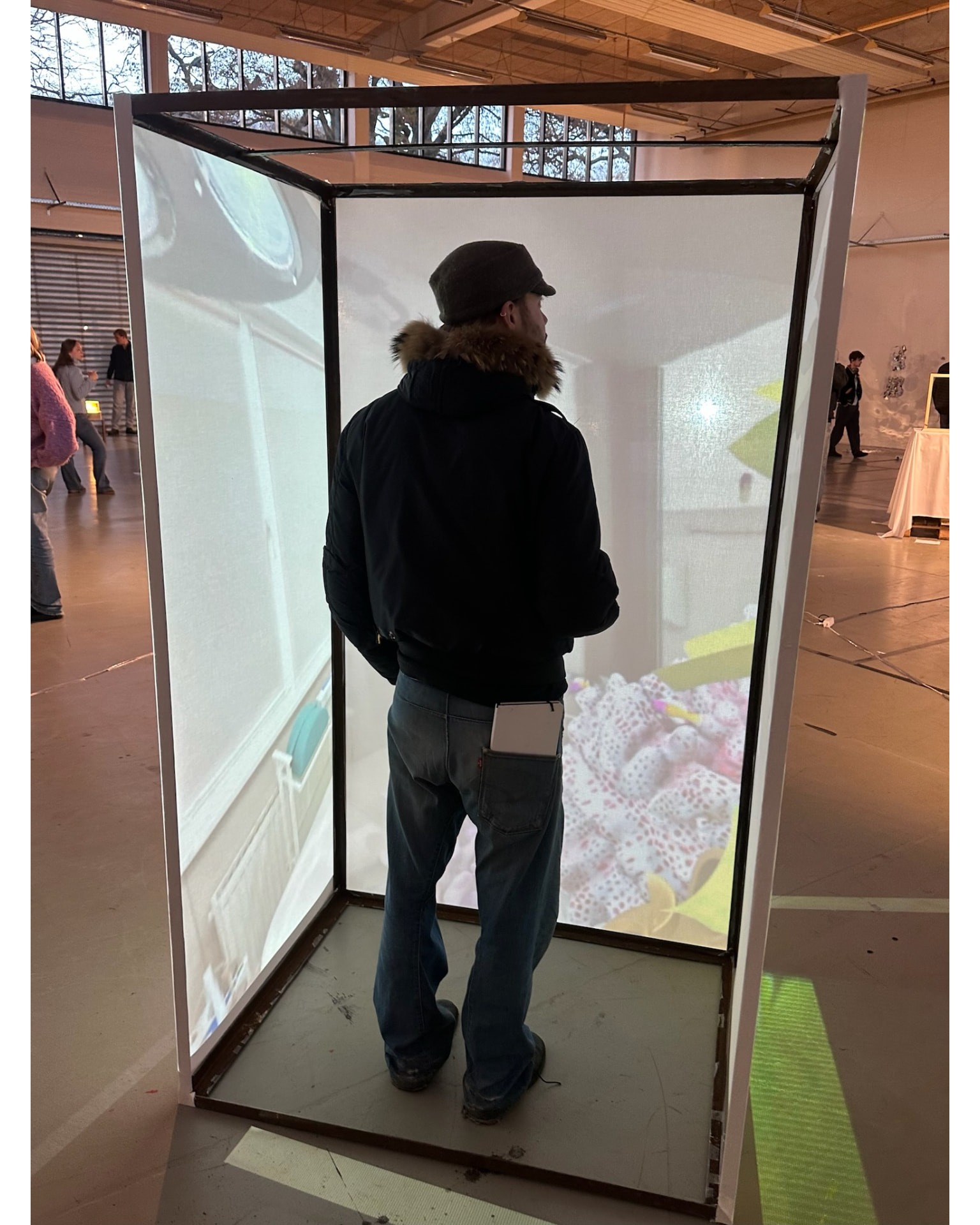 A visitor standing inside a translucent projection cube in an exhibition hall.