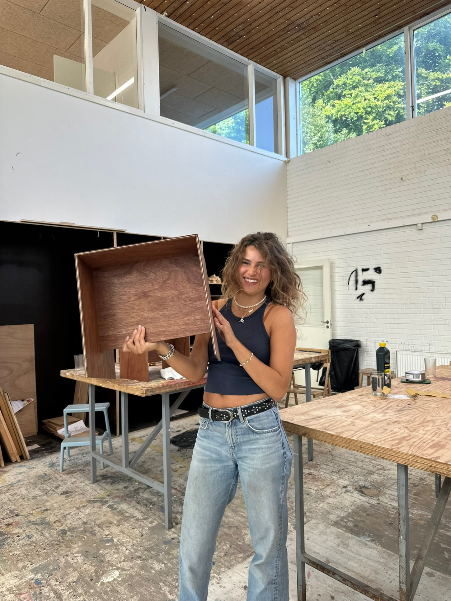 Lucca Lachmann holding a cabinet she has built in the workshop.