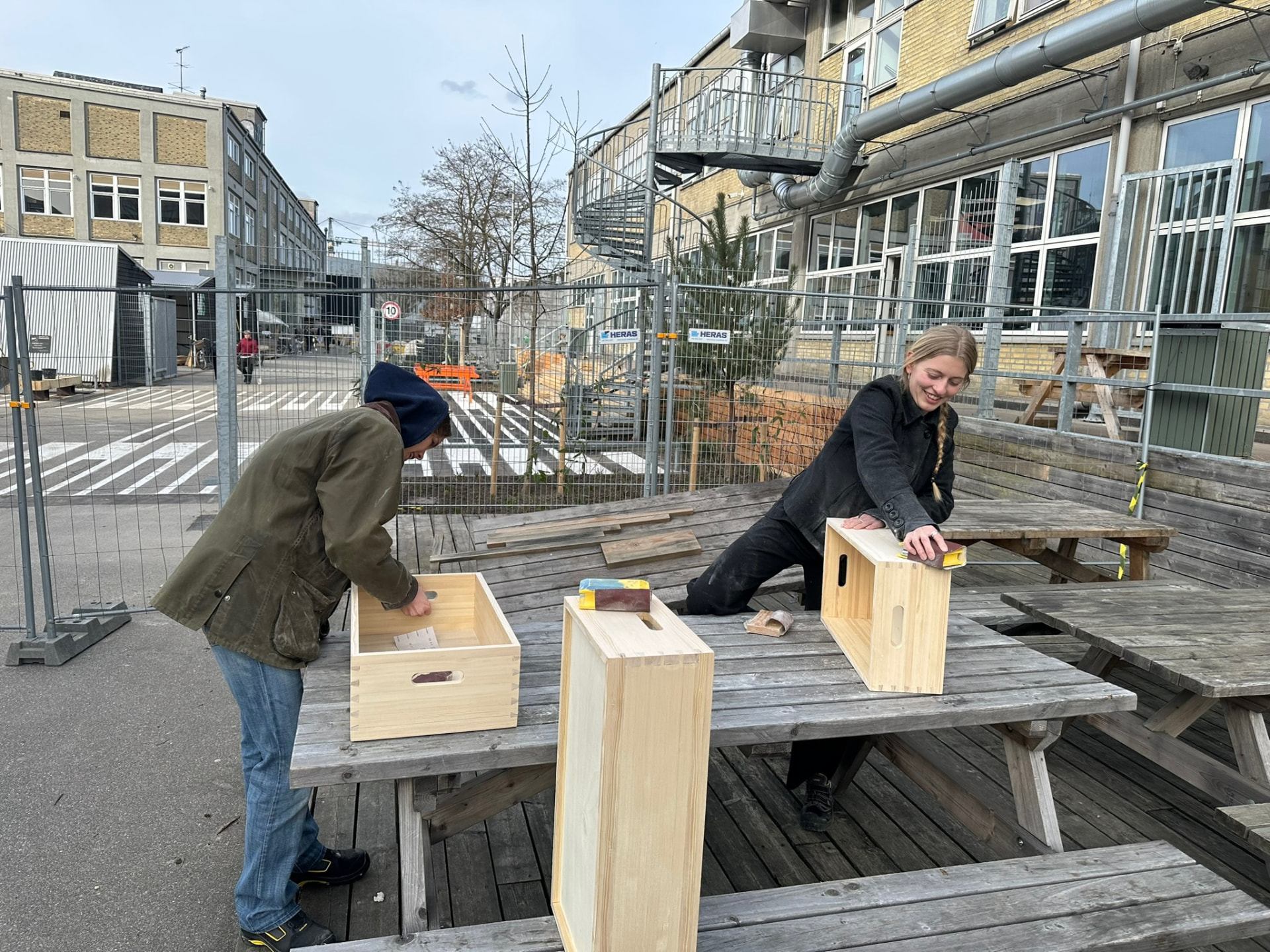 Two students sanding pine boxes on a picnic table in the yard outside the workshop.