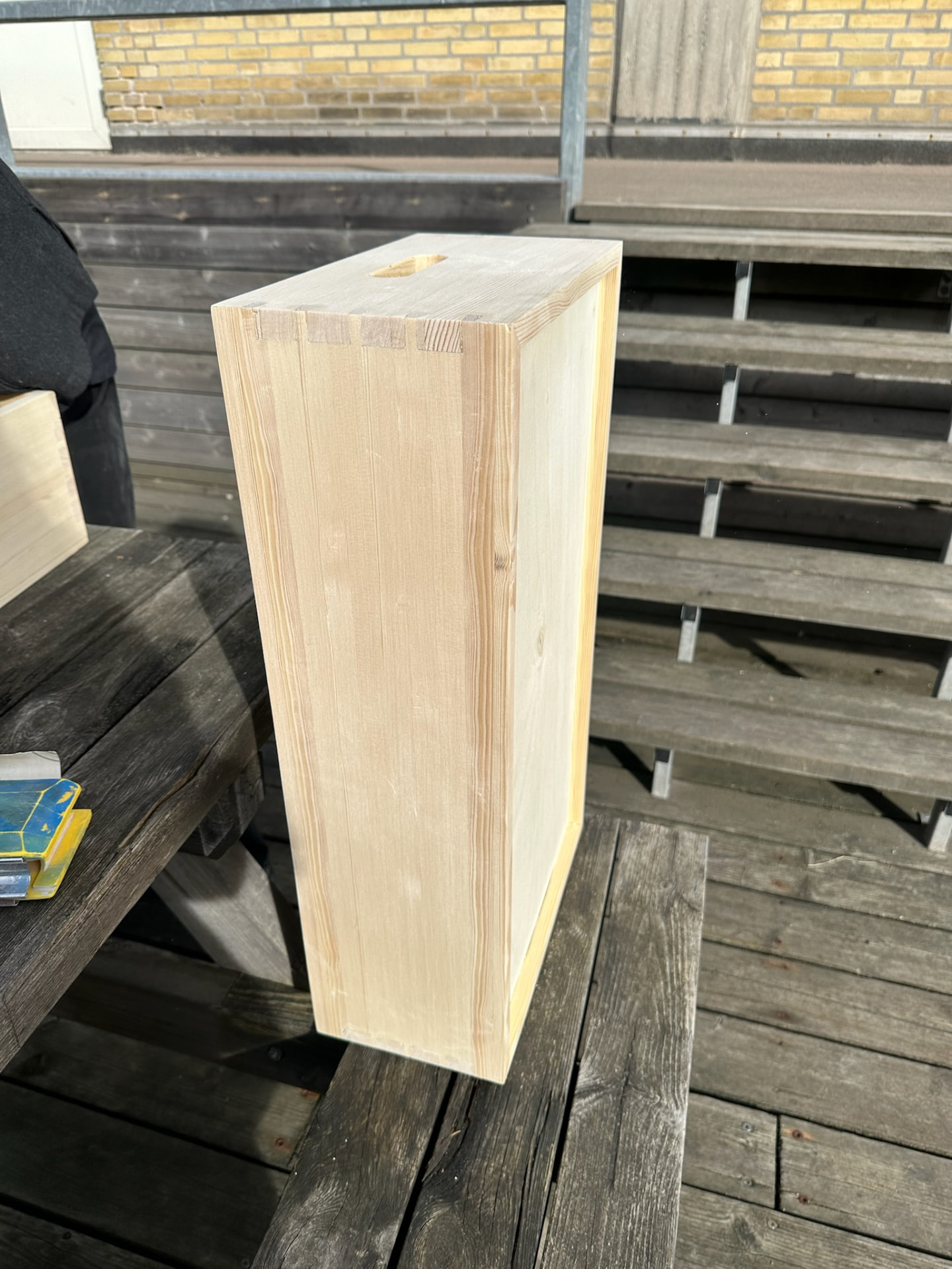 Finished pine box with dovetailed corners and a routed handle, standing on a bench outside.
