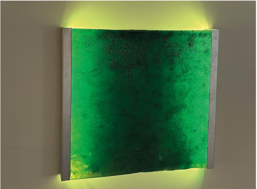 Wall-mounted lamp with a green bioplastic panel glowing against the wall.