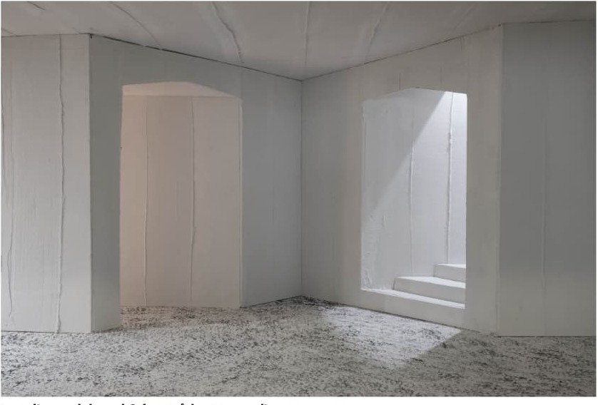 White architectural model interior with daylight falling through an opening onto a speckled floor.