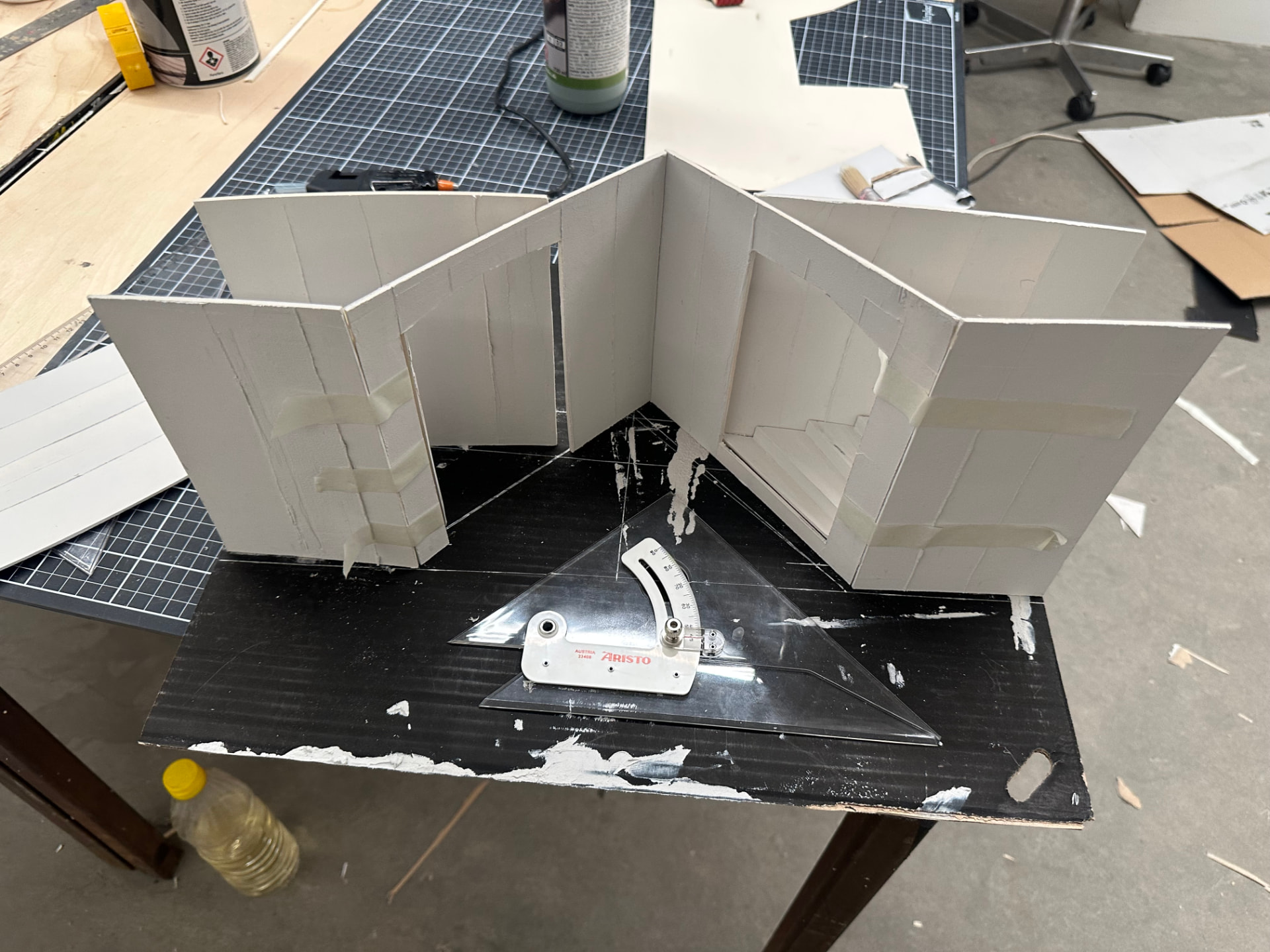 White foam board architectural model with an angle ruler on a cutting mat.