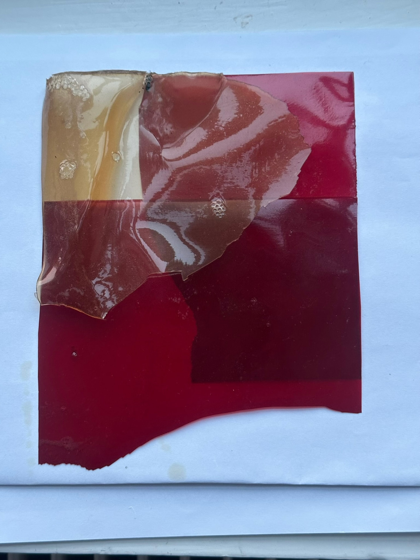Overlapping red and amber bioplastic sheets arranged on paper.