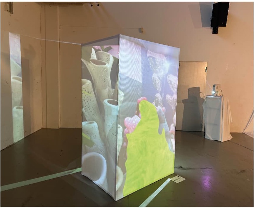 Projection installation forming a translucent cube with underwater imagery in a dark exhibition space.