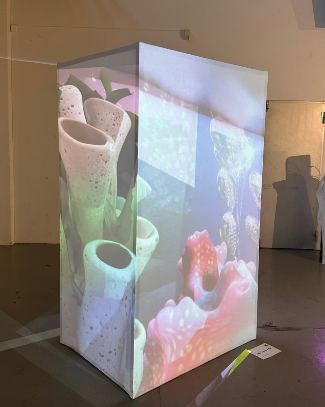 Translucent fabric cube in a gallery with ceramic vessels projected onto its surfaces.